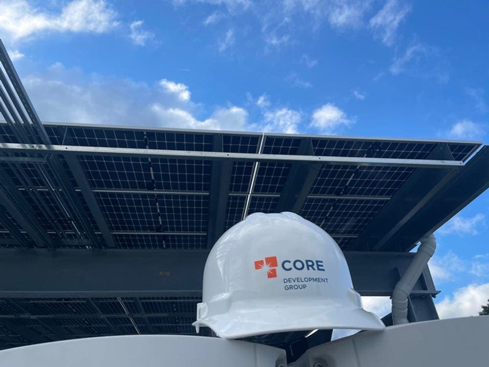 A white hard hat with the core development group logo on it with a solar panel in the background.